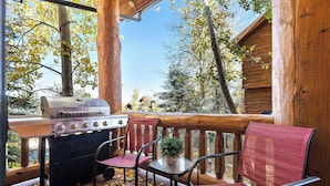 A wooden deck with a grill, chairs, and a small table.