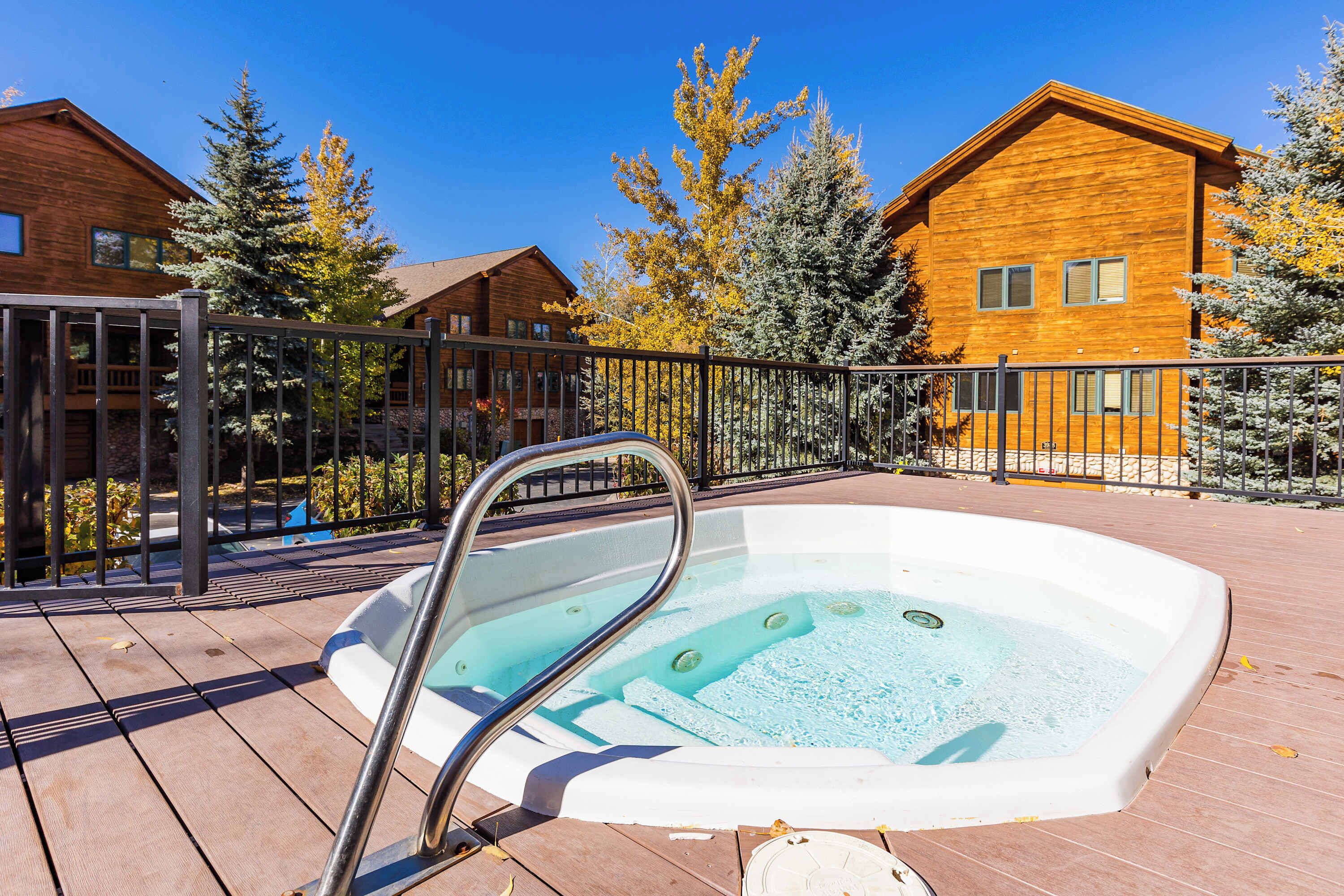 A wooden cabin with a hot tub on a deck, surrounded by trees and a clear blue sky.