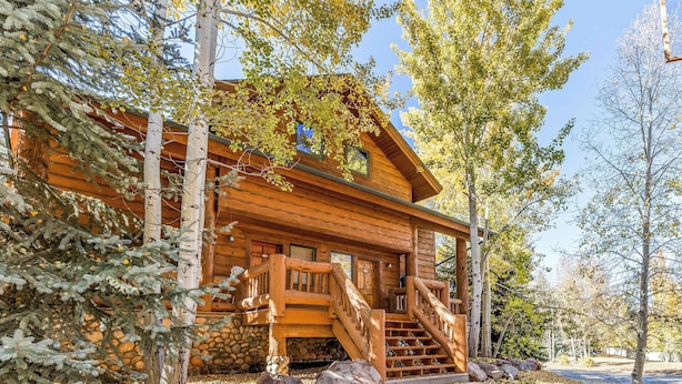 A log cabin with a wooden staircase leading to a porch, surrounded by trees and rocks.