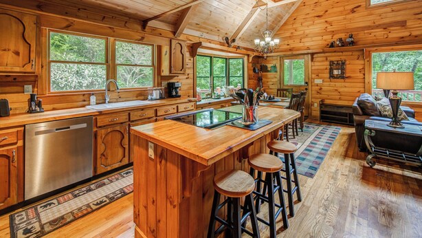 Interior de una cabaña de madera con cocina, comedor y barra.