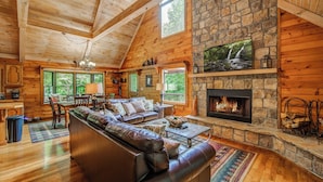 Interior acogedor de una cabaña con chimenea de piedra, paredes de madera y un ventanal con vistas a la vegetación.