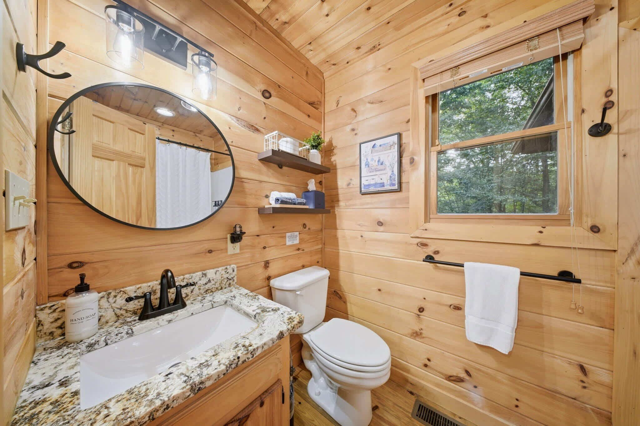 Bany d'una cabana de fusta amb un lavabo, vàter, mirall i finestra.