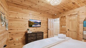 Une pièce aux murs lambrissés, contenant un lit, une commode et un tableau représentant un paysage de montagne.