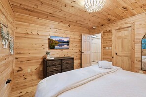 Una habitación con paneles de madera, una cama, un aparador y un cuadro de un paisaje montañoso.