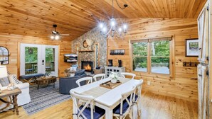 L’intérieur d’un chalet en bois comprend un coin repas, des sièges, une cheminée et de grandes fenêtres.
