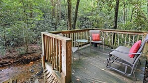 A wooden deck with a railing, two chairs, and a small table.
