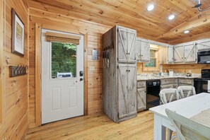 A wooden interior with a white door, a kitchen area with wooden cabinets, a dining table, and a hanging coat rack. - Cabin in Blue Ridge Hot Tub, Games, & Creek! (Blue Ridge)