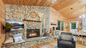 A cozy cabin interior with a stone fireplace, a comfortable seating area, and a dining space.