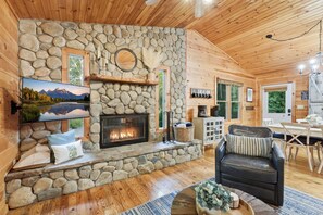 A cozy cabin interior with a stone fireplace, a comfortable seating area, and a dining space. - Cabin in Blue Ridge Hot Tub, Games, & Creek! (Blue Ridge)