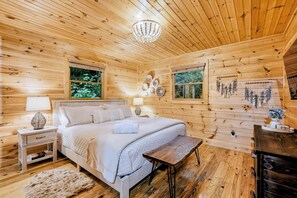 A wooden cabin bedroom with a bed, bedside tables, and a chandelier. - Cabin in Blue Ridge Hot Tub, Games, & Creek! (Blue Ridge)