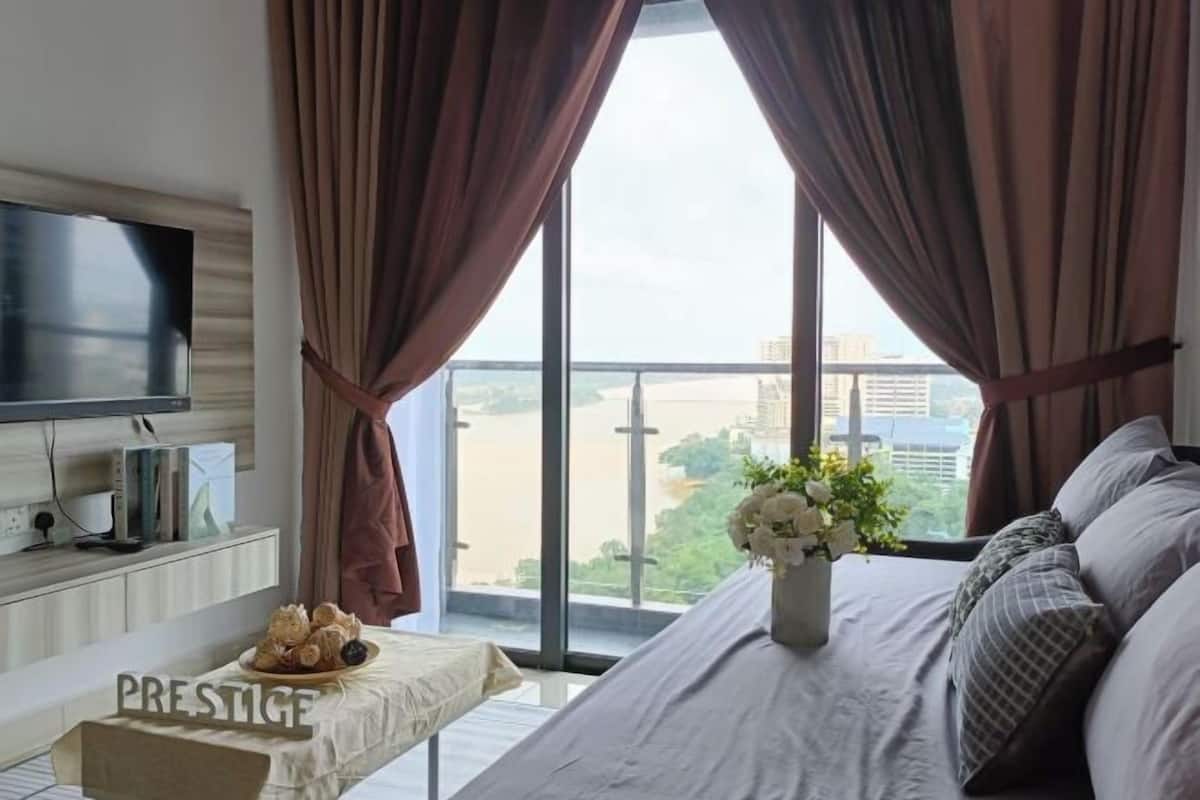 Un dormitorio con cama, televisor, una mesa con un cartel y vista a la ciudad.