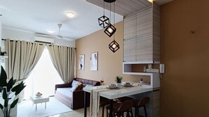 A modern living room with a sofa, a dining area with a table and chairs, a kitchen with cabinets, and a ceiling light fixture. - Prestige Sky Riverfront (Kota Bharu)