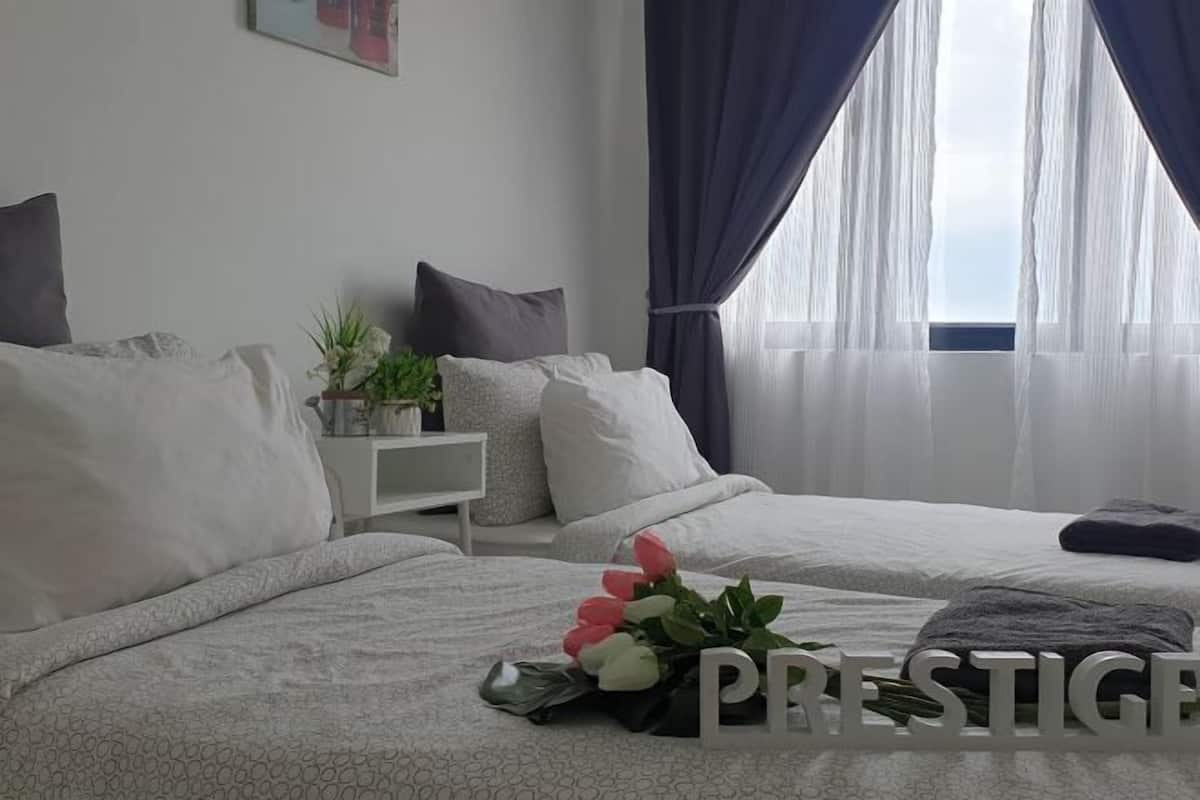 Un dormitorio con dos camas, una mesita de noche con una planta y una ventana con cortinas de gasa.