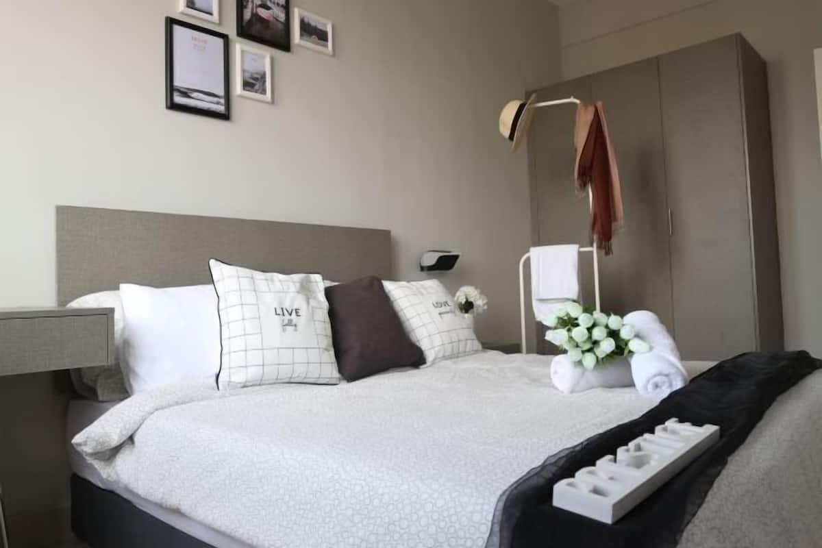Una cama bien hecha con almohadas, una mesita de noche, un armario y una pared con cuadros.