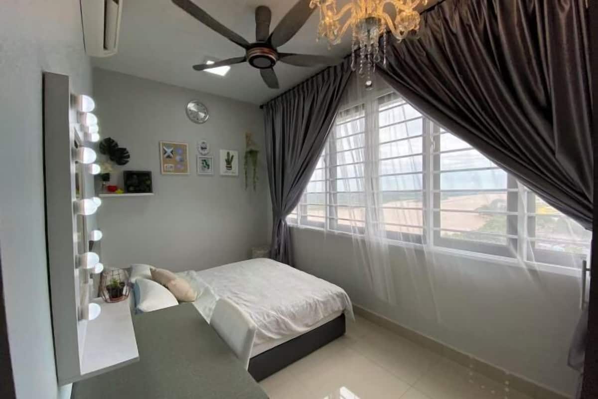 Un dormitorio con cama, tocador con luces, ventilador de techo y ventana con cortinas.