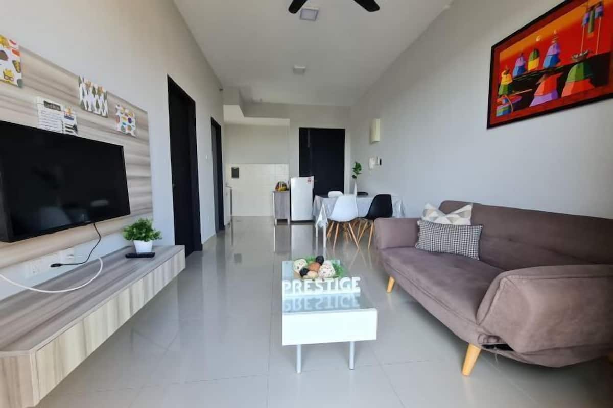 Una sala moderna con televisor de pantalla plana, un sofá, una mesa de centro y un comedor al fondo.