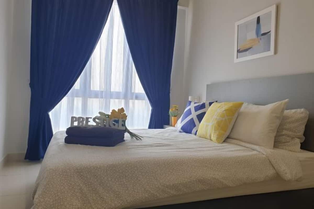 Una cama cuidadosamente hecha con una colcha blanca y beige estampada, almohadas azules y amarillas, y un letrero decorativo sobre la cama.