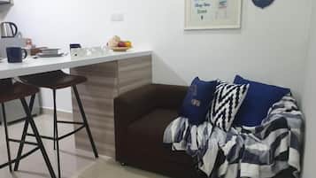 A small kitchenette with a white countertop, two bar stools, and a brown sofa with patterned cushions.