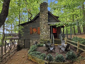 A rustic cabin with a stone chimney, wooden deck, and outdoor seating area surrounded by trees. - The Guest Cabin - Historic Home in Big Canoe (Big Canoe)