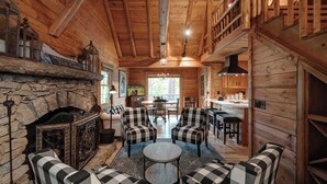 A cabin interior with a stone fireplace, checkered sofas, a round table, and a dining area with chairs. - The Guest Cabin - Historic Home in Big Canoe (Big Canoe)