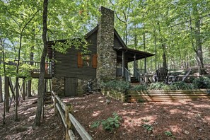 A rustic cabin with a stone chimney, wooden deck, and a covered porch.