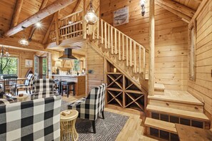 A wooden cabin interior with a dining area, checkered sofas, a staircase, and a kitchen. - The Guest Cabin - Historic Home in Big Canoe (Big Canoe)