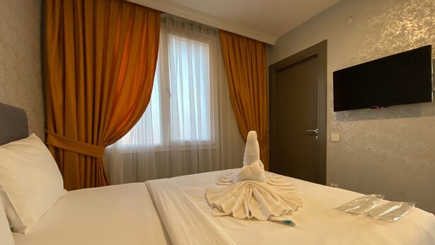 A hotel room with a neatly made bed, a flat-screen TV mounted on the wall, and a window with curtains. - PABLO SUIT AVCILAR (Istanbul)