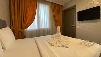 A hotel room with a neatly made bed, a flat-screen TV mounted on the wall, and a window with curtains.