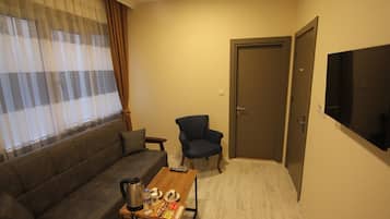 A compact living room with a sofa, armchair, coffee table, and a TV mounted on the wall.
