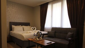 A hotel room with a bed, a sofa, a table with a tray of chocolates, a kettle, and a heart-shaped towel. - PABLO SUIT AVCILAR (Istanbul)