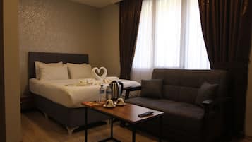 A hotel room with a bed, a sofa, a table with a tray of chocolates, a kettle, and a heart-shaped towel.