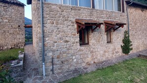 Ein Steinhaus mit geneigtem Dach und einem kleinen Fenster mit Holzläden.