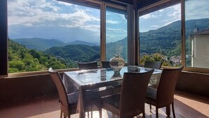 Ein geräumiger Balkon mit Glastisch und Korbstühlen, mit Blick auf eine gebirgige Landschaft.