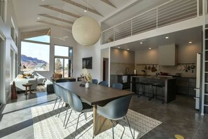 A modern kitchen with a central island, a dining area with a large table and chairs, and a view of the mountains through large windows. - Panoramic Views I Open Concept Floorplan I Private Hot Tub I Ample Parking (Moab)