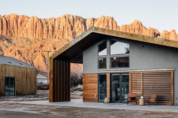 A modern building with large windows and a wooden exterior, set against a mountainous backdrop. - Panoramic Views I Open Concept Floorplan I Private Hot Tub I Ample Parking (Moab)