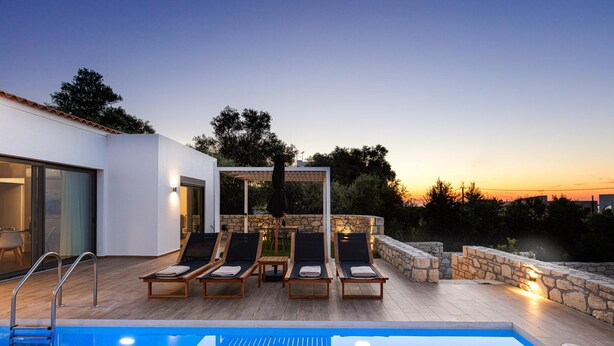 Un espace aménagé au bord de la piscine, avec des chaises longues, un mur en pierre et une vue sur le ciel.