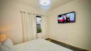 Quarto de hotel com cama grande, televisão na parede e janela com cortinas.