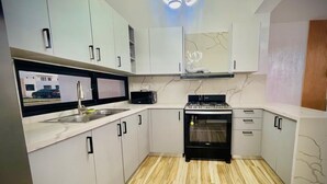 Uma cozinha compacta com armários brancos, fogão preto e painel de fundo de mármore.
