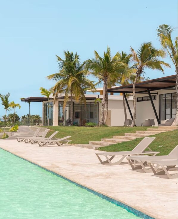 A modern resort with a swimming pool, lounge chairs, and palm trees.