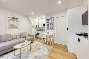 Cozy living space with a sofa, coffee table, and dining area, featuring a flat-screen TV and kitchenette.