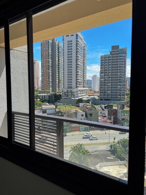 A high-rise building with multiple floors and balconies, viewed from a window with a metal frame. - Apto 1 dormitório no Brooklin  (São Paulo)