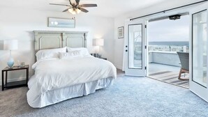 Un dormitorio con una cama grande, ventilador de techo, vista al océano y balcón con una silla.