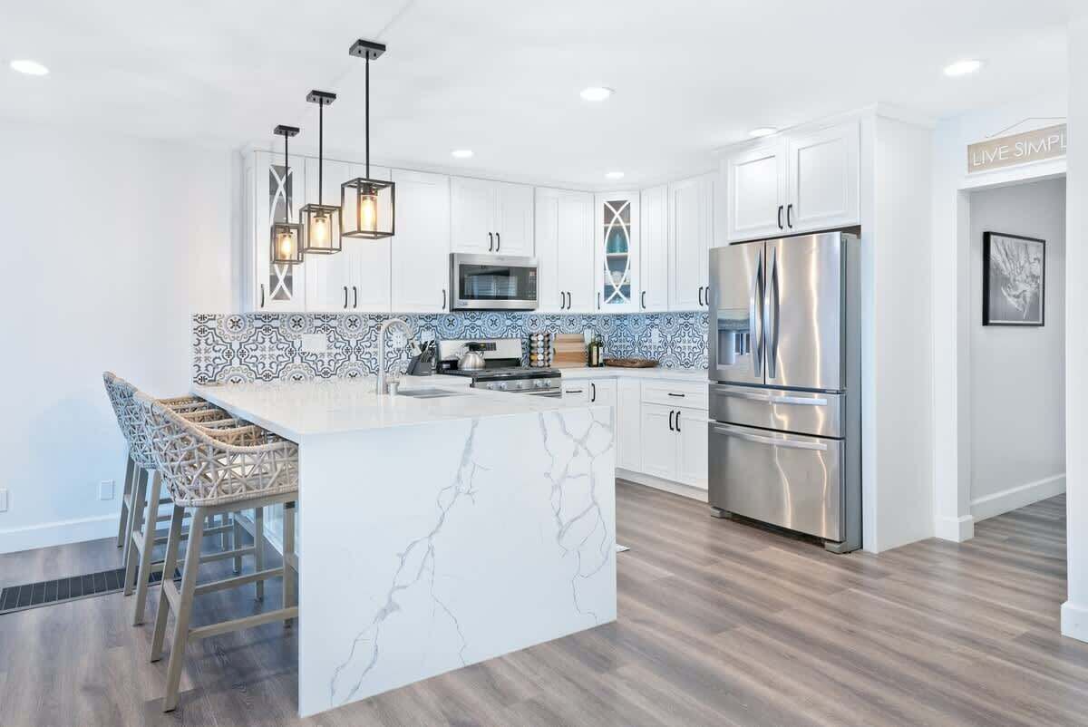 A modern kitchen with white cabinetry, a marble island, stainless steel appliances, and a patterned backsplash.