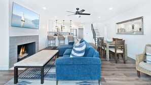 Una sala moderna con chimenea, un sofá, un comedor y una cocina al fondo.