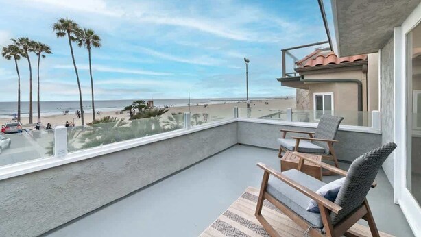 Un balcón con vista a la playa, palmeras y un cielo despejado.
