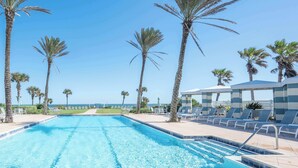 A swimming pool with clear blue water, surrounded by palm trees and lounge chairs.
