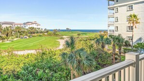 A golf course with a view of the ocean, surrounded by lush greenery and palm trees.