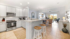 A modern kitchen with white cabinetry, a built-in microwave, and a large island with stools.