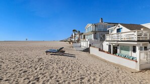 Una propiedad frente a la playa con una playa de arena, una silla de descanso y un edificio blanco de varios pisos con balcones.