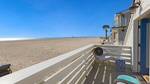 Un balcón con vista a la playa, una silla y una mesita.